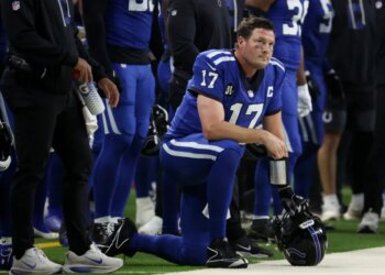 Indianapolis Colts quarterback Philip Rivers (17) on one knee looking on with his helmet in hand.