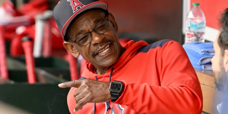 Ron Washington in a red hoodie and Los Angeles Angels cap, smiling and pointing in the dugout.