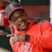 Ron Washington in a red hoodie and Los Angeles Angels cap, smiling and pointing in the dugout.