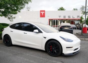 A white Tesla Model 3 car parked in front of a Tesla dealership.