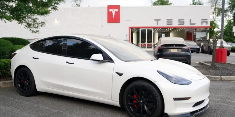 A white Tesla Model 3 car parked in front of a Tesla dealership.
