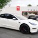 A white Tesla Model 3 car parked in front of a Tesla dealership.