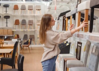A young woman comparing chairs on display in a furniture store.