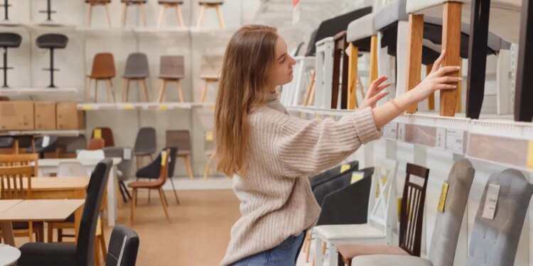 A young woman comparing chairs on display in a furniture store.