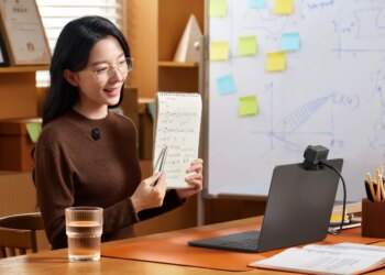 A person holds up a notebook to the Lyra webcam on a laptop while wearing a wireless lav mic.