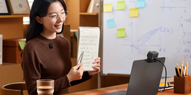 A person holds up a notebook to the Lyra webcam on a laptop while wearing a wireless lav mic.