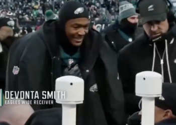 Jalen Hurts smiling on the sideline of a football game.