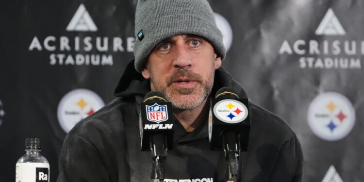 A man wearing a grey beanie and a dark hoodie, speaking into two microphones with NFL and Steelers logos.