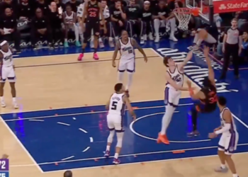 A basketball player in a black and red uniform dunks the ball into a hoop.