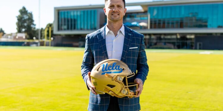 UCLA Football Head Coach Bob Chesney holding a gold helmet with "UCLA" written on it in blue.