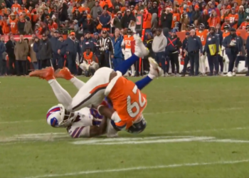 A Bills player in white and a Broncos player in orange tackle each other on a football field.