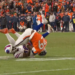 A Bills player in white and a Broncos player in orange tackle each other on a football field.