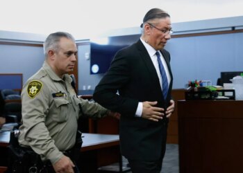 Nathan Chasing Horse, wearing a suit, is led from a courtroom by an officer in uniform.