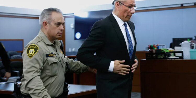 Nathan Chasing Horse, wearing a suit, is led from a courtroom by an officer in uniform.