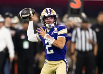 A Boise State Washington football player in a purple jersey and gold helmet throwing a football.