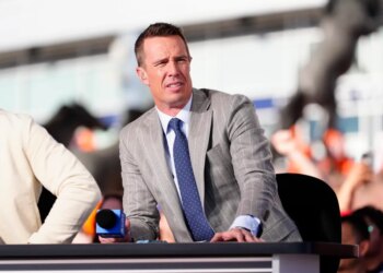 A man in a pinstripe suit and blue tie speaking into a microphone.