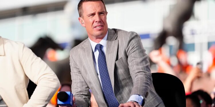 A man in a pinstripe suit and blue tie speaking into a microphone.