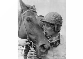 Diane Crump, wearing a jockey helmet, kisses her horse Tou Ritzi, who is bridled.