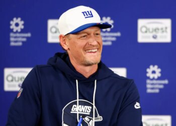 Interim defensive coordinator Charlie Bullen smiling while wearing a Giants cap and hoodie during football practice.