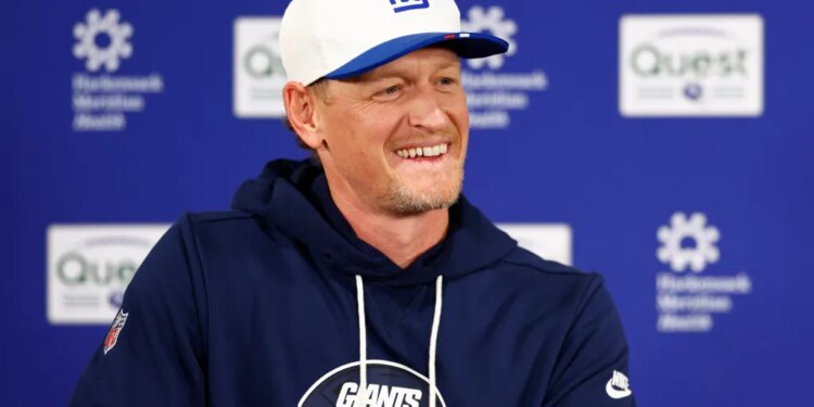 Interim defensive coordinator Charlie Bullen smiling while wearing a Giants cap and hoodie during football practice.