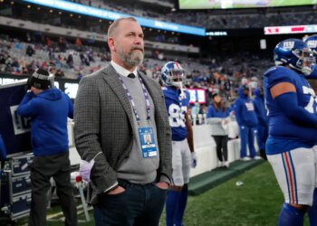 Kevin Abrams, New York Giants executive, wearing a grey jacket, sweater, and white collared shirt, stands on the sidelines of MetLife Stadium.