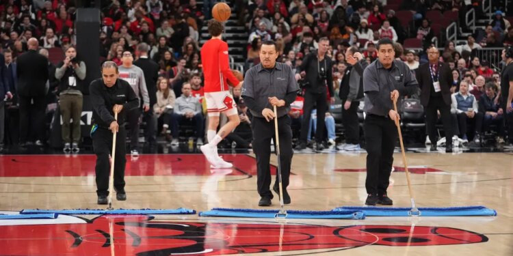 Three arena employees mop the basketball court during an NBA game.
