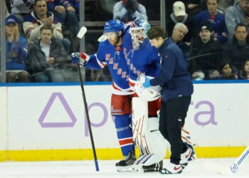 New York Rangers goaltender Igor Shesterkin is helped off the ice by a trainer and New York Rangers defenseman Vladislav Gavrikov.