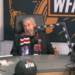 A man wearing a New York Rangers scarf sits at a desk with a WFAN microphone, a basketball, and a football helmet, all branded with WFAN.