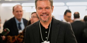 Actor Matt Damon smiling while wearing a conference badge around his neck at the World Economic Forum.