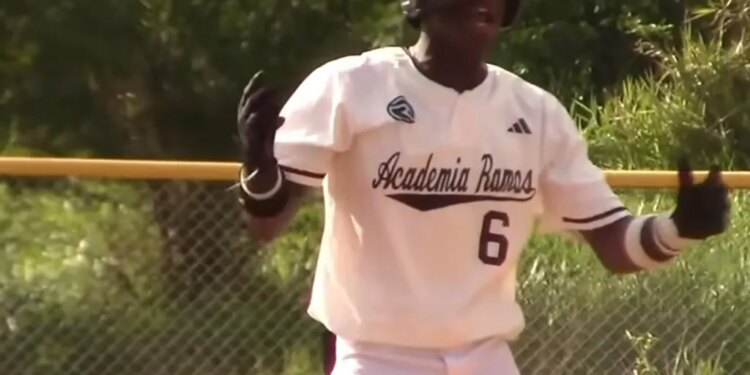 Baseball player Wandy Asigen in a white uniform and helmet, with "Academia Ramos 6" on his back, gesturing excitedly.