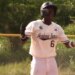 Baseball player Wandy Asigen in a white uniform and helmet, with "Academia Ramos 6" on his back, gesturing excitedly.