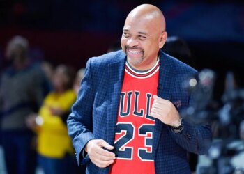 Michael Wilbon, coach of Team Wilbon, smiles while wearing a red Chicago Bulls jersey and a dark blue blazer.
