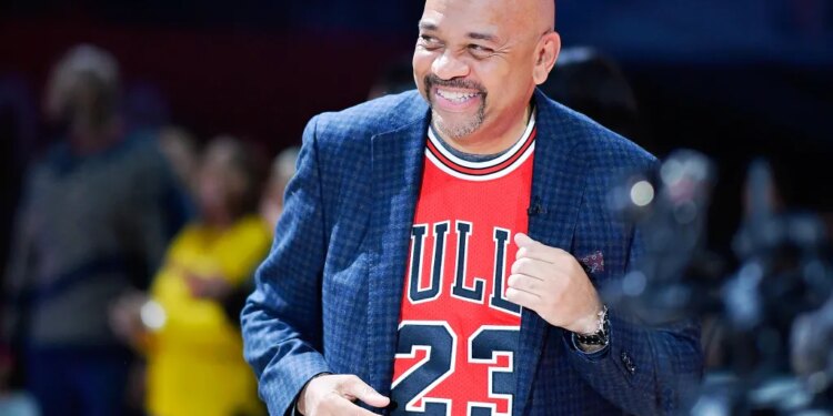 Michael Wilbon, coach of Team Wilbon, smiles while wearing a red Chicago Bulls jersey and a dark blue blazer.