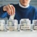 Man putting money into a jar labeled "House," among jars labeled "Car," "Education," and "Investment."