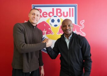 Two men shaking hands in front of a Red Bull logo with a soccer ball.