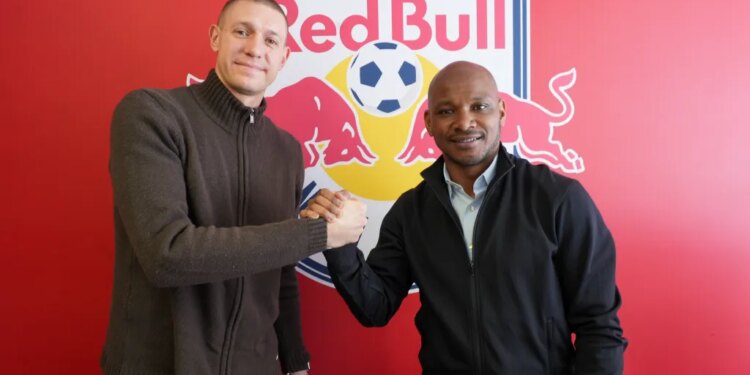 Two men shaking hands in front of a Red Bull logo with a soccer ball.