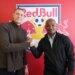 Two men shaking hands in front of a Red Bull logo with a soccer ball.