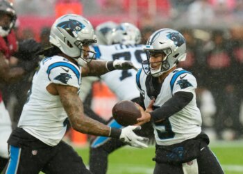 Carolina Panthers quarterback Sam Darnold handing off the ball to running back D'Onta Foreman in a rainy game.