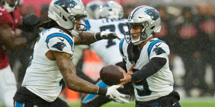 Carolina Panthers quarterback Sam Darnold handing off the ball to running back D'Onta Foreman in a rainy game.