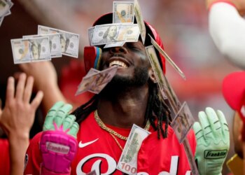 Cincinnati Reds player Elly De La Cruz in the dugout, showered with play money by teammates.