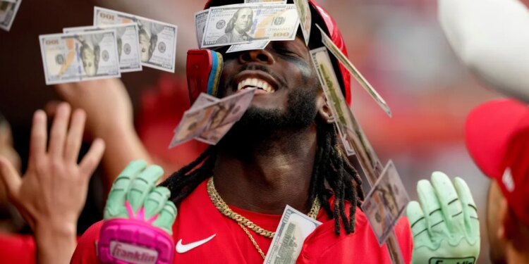 Cincinnati Reds player Elly De La Cruz in the dugout, showered with play money by teammates.