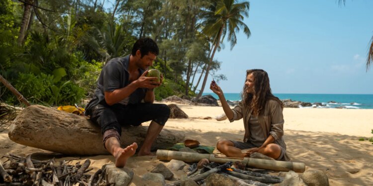 A man and a woman sitting on a beach in front of a makeshift fire pit.