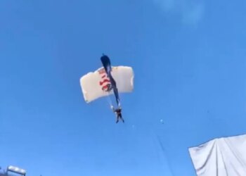 A parachuter with a white and blue parachute caught in a field goal net above a stadium.