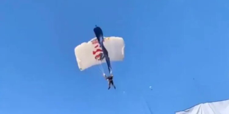 A parachuter with a white and blue parachute caught in a field goal net above a stadium.