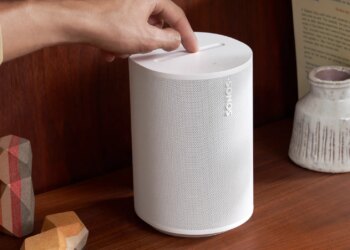 A marketing image of the Sonos Era 100 speaker on a wood shelf.