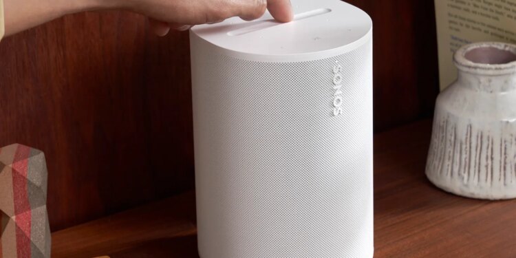 A marketing image of the Sonos Era 100 speaker on a wood shelf.