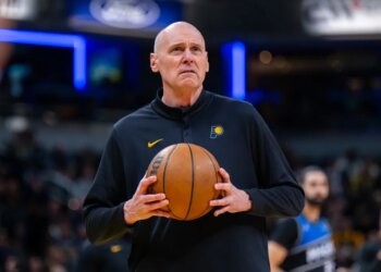 Indiana Pacers head coach Rick Carlisle looking toward the scoreboard while holding a basketball.