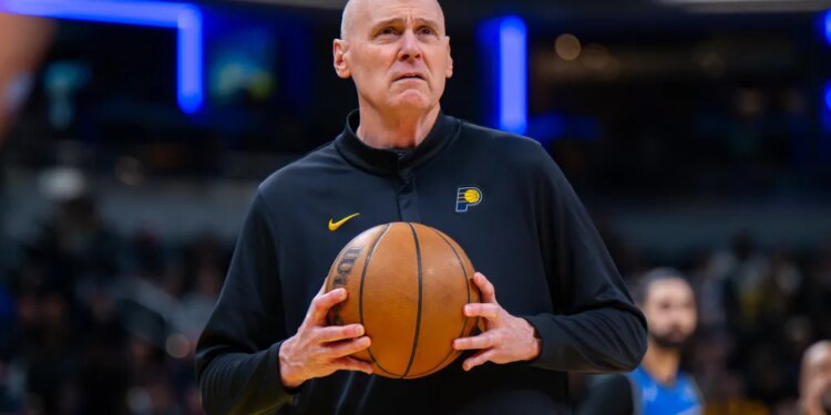 Indiana Pacers head coach Rick Carlisle looking toward the scoreboard while holding a basketball.