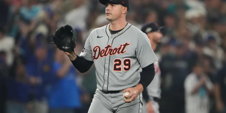 A baseball player in a gray "Detroit 29" jersey, black cap, and black glove holds a baseball.