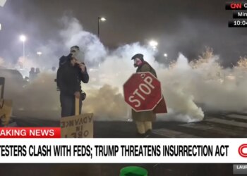 People covered in smoke, one holding a stop sign, at a protest where federal agents deployed tear gas.